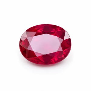 Puede incluir: Una gema de rubí de corte ovalado con un color rojo intenso y saturado. La piedra muestra una superficie facetada con múltiples facetas triangulares y en forma de cometa que reflejan la luz, creando una apariencia brillante y pulida.