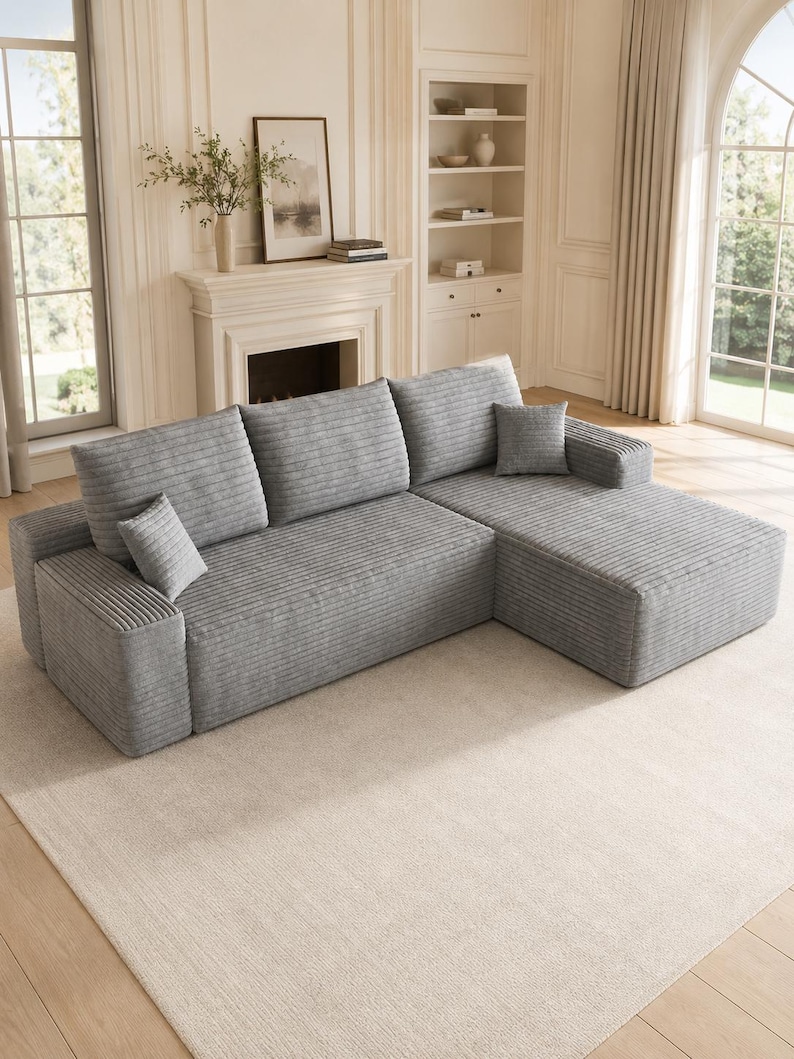 May include: A light gray sectional sofa featuring a textured corduroy fabric, three large back cushions, a chaise lounge section on the right side, and two small square throw pillows placed on the seat cushions.