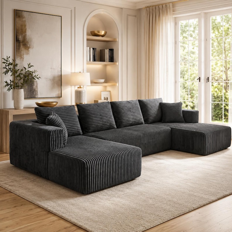Op de afbeelding: Een grote antracietgrijze hoekbank met een bekleding van gestructureerde corduroy stof. Dit modulaire meubelstuk is voorzien van een chaise longue, diepe zitkussens en diverse bijpassende vierkante sierkussens in dezelfde stof.