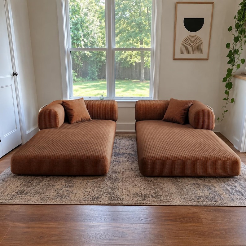 May include: Two low-profile, armless chaise lounge chairs upholstered in a textured, rust-colored corduroy fabric. Each piece features a single rounded bolster-style armrest on the outer side and includes one matching square throw pillow.