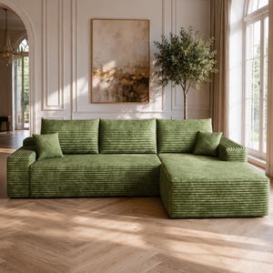 May include: A large, L-shaped sectional sofa upholstered in a textured, olive green corduroy fabric. The sofa features a long chaise lounge on the right side, three wide back cushions, and two small, square throw pillows in the same green fabric.