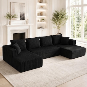 Op de afbeelding: Een grote zwarte hoekbank van gestructureerde corduroy stof. De bank heeft een U-vormige configuratie met twee verlengde chaise longue-gedeelten, diepe zittingen, meerdere bijpassende vierkante rugkussens en &eacute;&eacute;n klein sierkussen.