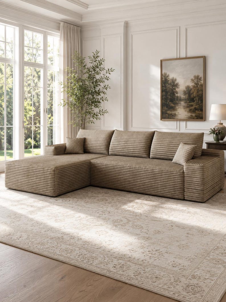 May include: A large, L-shaped sectional sofa upholstered in a textured, light brown corduroy fabric. The sofa features a chaise lounge on the left side, three wide back cushions, and two small square throw pillows in the same matching fabric.