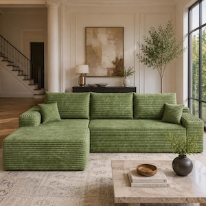 May include: A large, L-shaped sectional sofa upholstered in a textured, ribbed green fabric. The sofa features a chaise lounge on the left side, three back cushions, and two small square throw pillows placed at each end of the seating area.