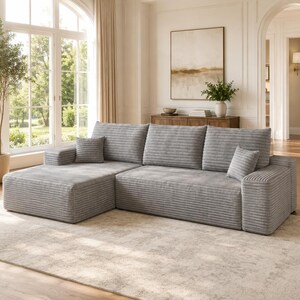 May include: A light gray sectional sofa featuring a textured corduroy fabric, a chaise lounge on the left side, three large back cushions, and two small square throw pillows. The sofa has a low-profile design with wide, flat armrests.