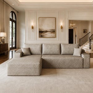 May include: A large, beige sectional sofa featuring a horizontal ribbed texture across the cushions and frame. The sofa includes a chaise lounge section on the left side and two small, matching square throw pillows placed on the seat cushions.