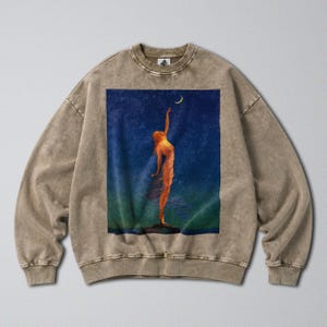 May include: A mineral-washed brown crewneck sweatshirt featuring a rectangular graphic print on the chest. The artwork depicts a figure standing on a rock, reaching toward a yellow crescent moon against a dark blue and green night sky background.