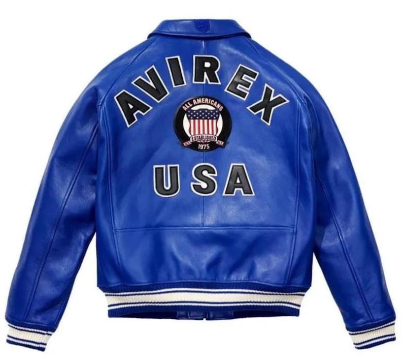 Puede incluir: Una chaqueta de cuero azul brillante con cuello cl&aacute;sico y mangas largas. La parte posterior muestra el texto AVIREX en letras negras, un parche circular con un dise&ntilde;o de bandera estadounidense y el texto USA en letras negras con bordes blancos.