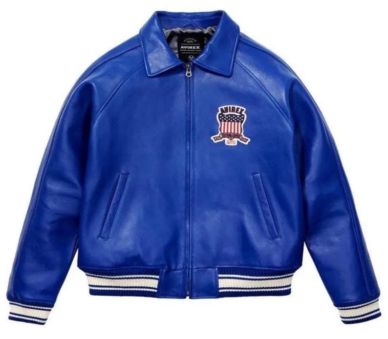 Puede incluir: Una chaqueta de cuero azul vibrante con cuello cl&aacute;sico, cremallera frontal completa y dos bolsillos laterales. El pecho muestra un parche bordado con el texto AVIREX y un gr&aacute;fico de escudo. Los pu&ntilde;os y el dobladillo tienen rayas blancas y azules.