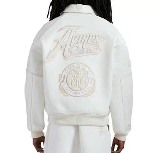 May include: A white varsity-style jacket featuring a large embroidered Avirex New York logo on the back. Below the text is a circular patch with the text Avirex Gold Club NYC. The jacket has ribbed cuffs and hem, with textured panels on the sleeves.