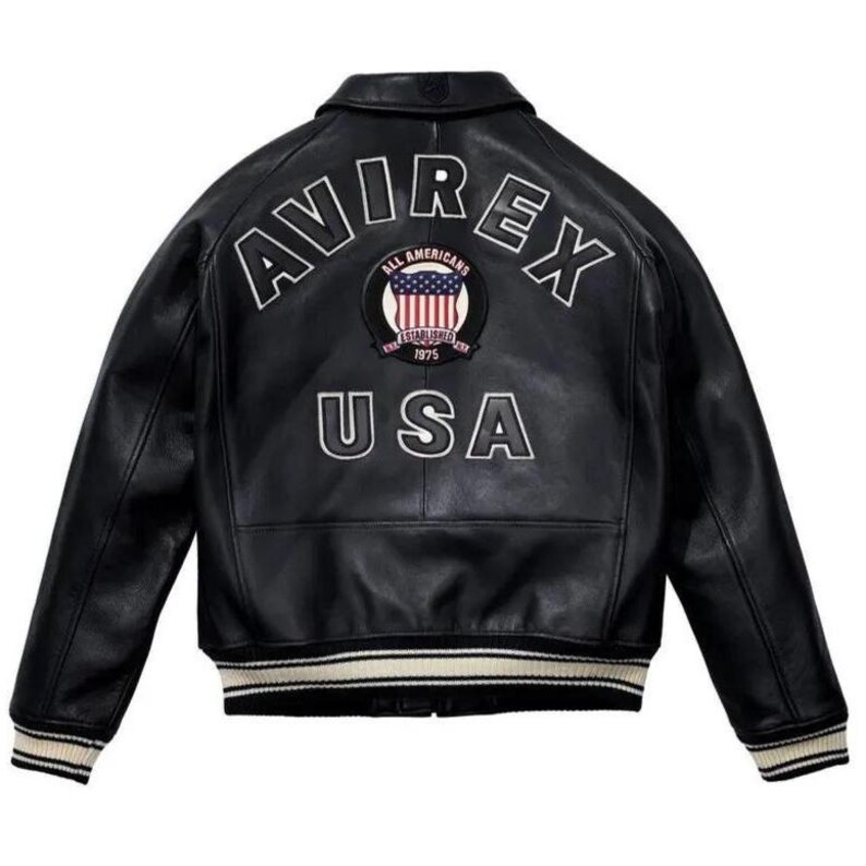 May include: A black leather varsity jacket featuring the text AVIREX in white arched lettering across the upper back. Below the text is a circular patch with an American flag design and the text ALL AMERICANS ESTABLISHED 1975. USA is printed below.