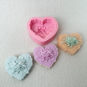 May include: A pink heart-shaped silicone mold with a detailed floral lace texture, accompanied by three finished heart-shaped items in light blue, lavender, and peach, each featuring a raised rose bouquet design and intricate lace detailing.