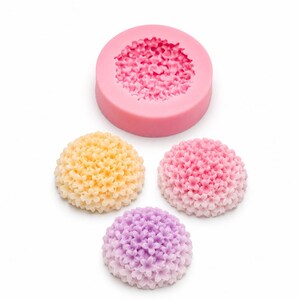 May include: A round pink silicone mold featuring a detailed floral texture, accompanied by three dome-shaped floral castings in yellow, pink, and purple. Each casting displays a dense cluster of small, five-petaled flowers in a rounded arrangement.