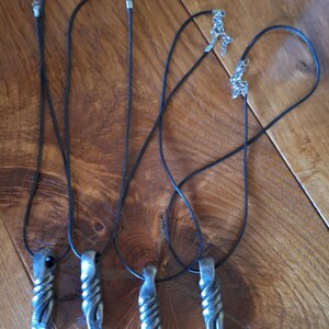 Peut inclure: Quatre colliers pendentifs en métal faits à la main avec des cordons noirs et des fermoirs argentés. Les pendentifs ont un design torsadé et texturé et une forme pointue. Les colliers sont présentés sur une surface en bois.