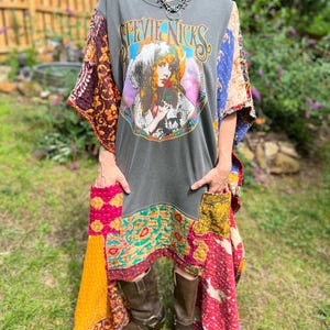 May include: A charcoal gray t-shirt dress featuring a graphic print of Stevie Nicks with the text "STEVIE NICKS" above her image. The dress is accented with multicolored, quilted fabric patches on the sleeves and hem, including two front pockets.
