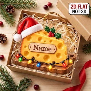 May include: A 2D flat Christmas ornament shaped like a wedge of Swiss cheese with holes, wearing a red Santa hat and green holly. It features a central plaque with the text Name, a string of colorful lights, and a gold hanging cord.