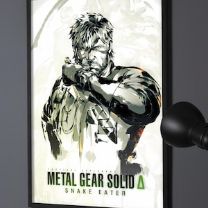 Puede incluir: Un póster enmarcado con una ilustración en tinta negra y blanca de un personaje con pelo corto y barba, vistiendo equipo táctico. El texto dice TACTICAL ESPIONAGE ACTION METAL GEAR SOLID DELTA SNAKE EATER en negro y verde.