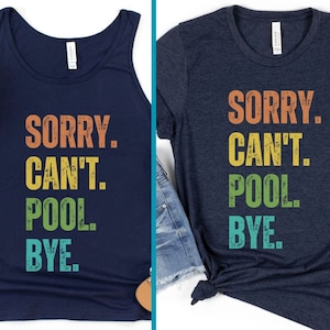 Puede incluir: Dos camisas azul marino con el texto "SORRY. CAN'T. POOL. BYE." en una fuente retro y desgastada. El texto está en diferentes colores, incluyendo naranja, amarillo, verde y azul.
