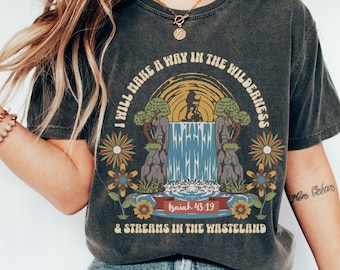 May include: A dark grey t-shirt with a vintage-style graphic of a waterfall in a forest. The graphic includes the text "I will make a way in the wilderness & streams in the wasteland" and "Isaiah 43:19".