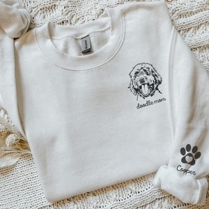 Może przedstawiać: Biała bluza z okrągłym dekoltem z nadrukiem "doodle mom" i odciskiem łapy z imieniem Cooper na rękawie.