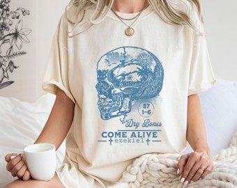 May include: A cream coloured t-shirt with a blue skull graphic and the text "37 Dry Bones 1-6 Come Alive -+ ezekiel +-"