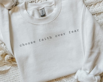 May include: White crewneck sweatshirt with the text "choose faith over fear" printed in black on the front.