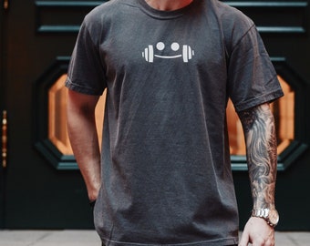 Può includere: Una t-shirt color grigio scuro melange con una grafica bianca di un viso sorridente con cuffie. Il testo "Dark Grey Heather" è visibile nella parte inferiore dell'immagine.