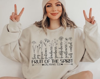 Puede incluir: Una sudadera beige con un gráfico negro de flores y el texto "FRUIT OF THE SPIRIT GALATIANS 5:22".