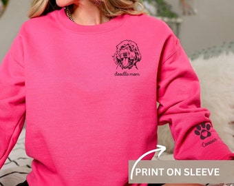 May include: Pink sweatshirt with a doodle dog graphic on the front and the text "doodle mom". The sleeve has a paw print graphic with the name "Cooper" printed below it.
