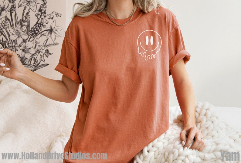 May include: A rust-colored t-shirt with a white dripping smiley face graphic.