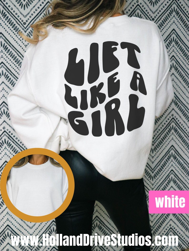 Puede incluir: Sudadera blanca con texto negro que dice "Lift Like A Girl" en la espalda. La sudadera se muestra en una modelo con pantalones negros.