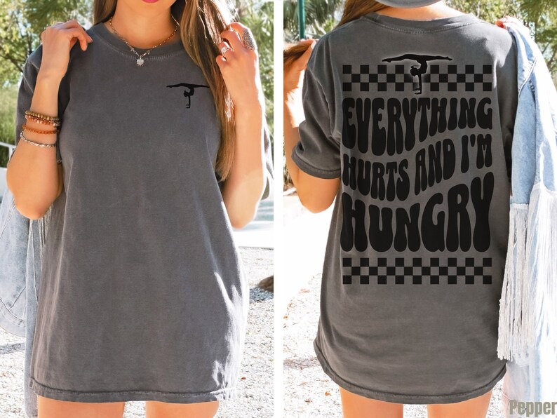 K&ouml;nnte beinhalten: Graues Oversize-T-Shirt mit einer Turner-Silhouette auf der Vorderseite und dem Text "Everything Hurts and I'm Hungry" auf der R&uuml;ckseite. Der Text ist in einer Retro-Schriftart mit einem karierten Muster.