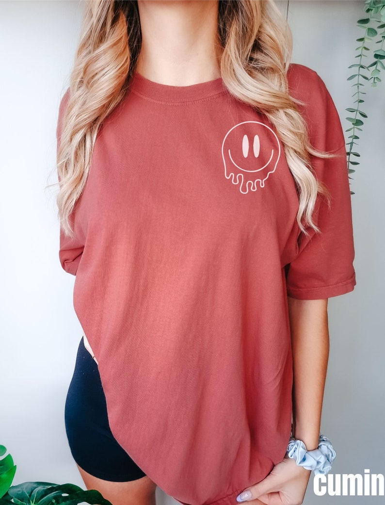 May include: A rust-colored t-shirt with a white dripping smiley face graphic.