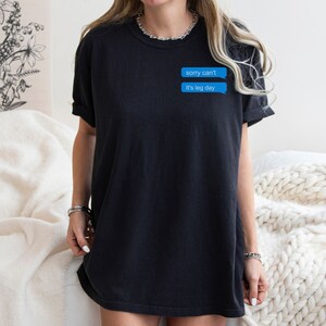 Może przedstawiać: Czarny, oversize'owy t-shirt z niebieskim nadrukiem wiadomości tekstowej, na kt&oacute;rym widnieje napis "sorry can't it's leg day"