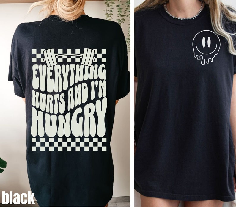 May include: Black t-shirt with a white graphic on the back that says "Everything Hurts and I'm Hungry" with a dumbbell and checkered pattern. The front of the shirt has a white dripping smiley face graphic.