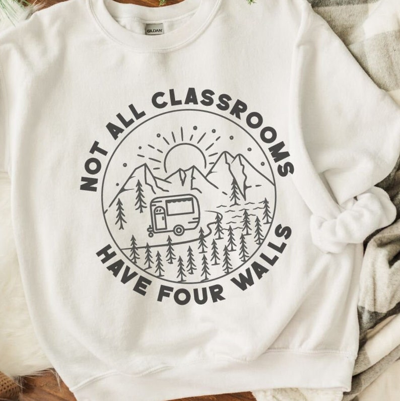 K&ouml;nnte beinhalten: Wei&szlig;es Sweatshirt mit einem schwarz-wei&szlig;en Grafikdesign eines Wohnmobils, das durch eine Berglandschaft f&auml;hrt. Der Text "Not all classrooms have four walls" ist in einem Kreis um die Grafik gedruckt.