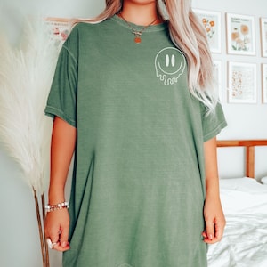 May include: A green oversized t-shirt with a white dripping smiley face graphic. The shirt is made of a soft, comfortable material.