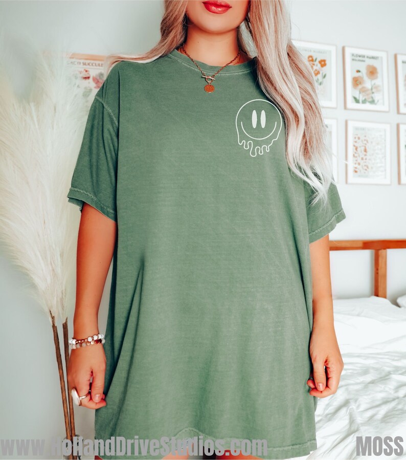 May include: A green oversized t-shirt with a white dripping smiley face graphic. The shirt is made of a soft, comfortable material.