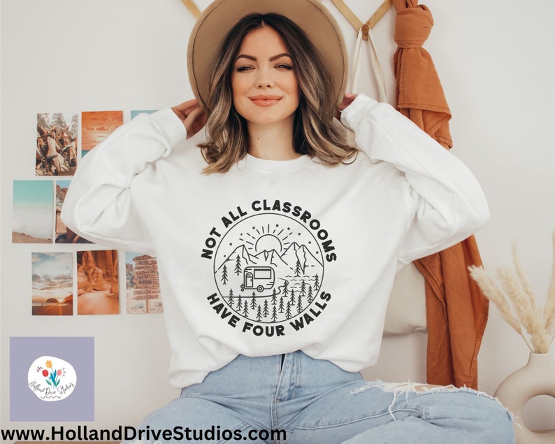 K&ouml;nnte beinhalten: Wei&szlig;er Pullover mit einem schwarzen Grafikdesign eines Wohnmobils vor Bergen und B&auml;umen. Der Text um die Grafik lautet "Not all classrooms have four walls".