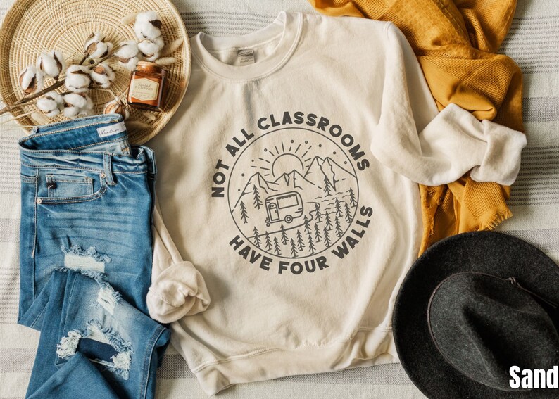 K&ouml;nnte beinhalten: Ein beiger Pullover mit einem grafischen Design eines Wohnmobils in einer Berglandschaft. Der Text lautet "Not all classrooms have four walls".
