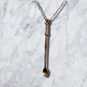 May include: A copper-toned pendant shaped like a long, slender spoon with a textured, branch-like handle. The pendant hangs from a silver-coloured metal ball chain, featuring a small loop at the top for attachment to the chain, creating a unique necklace.