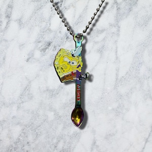 May include: A rainbow-coloured metal spoon pendant on a silver-toned ball chain. The spoon features a yellow Spongebob Squarepants character graphic and the red text KRUSTY printed vertically along the handle, creating a unique accessory piece.
