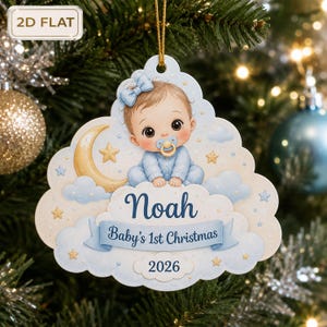 Puede incluir: Un adorno navideño plano con forma de nube que muestra a un bebé con un lazo azul y un chupete sentado sobre una luna creciente. El adorno presenta el nombre Noah, el texto Baby's 1st Christmas y el año 2026 en azul sobre fondo celeste.