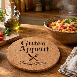 Könnte beinhalten: Ein runder Untersetzer aus Kork mit der Aufschrift "Guten Appetit" und einem Messer- und Gabel-Design. Der Untersetzer liegt auf einem Holztisch neben einer Schüssel Pasta.