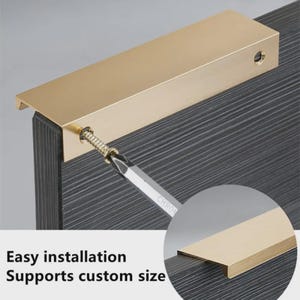 May include: A gold-colored metal edge pull handle mounted on a dark gray textured cabinet door. A screwdriver is shown inserting a screw into the handle. The text on the image reads: Easy installation, Supports custom size.