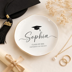 Könnte beinhalten: Eine runde weiße Keramikschale mit goldenem Rand. In der Mitte befindet sich ein schwarzes Doktorhut-Symbol, der Name Sophia in Schreibschrift und der Text CLASS OF 2026 UNIVERSITY OF CHICAGO in einer serifenlosen Schriftart.