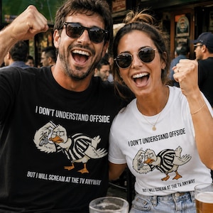 Puede incluir: Un hombre y una mujer con camisetas blancas y negras con el texto "I DON'T UNDERSTAND OFFSIDE BUT I WILL SCREAM AT THE TV ANYWAY". Las camisetas presentan un pato de dibujos animados con uniforme de árbitro. Ambos sonríen.