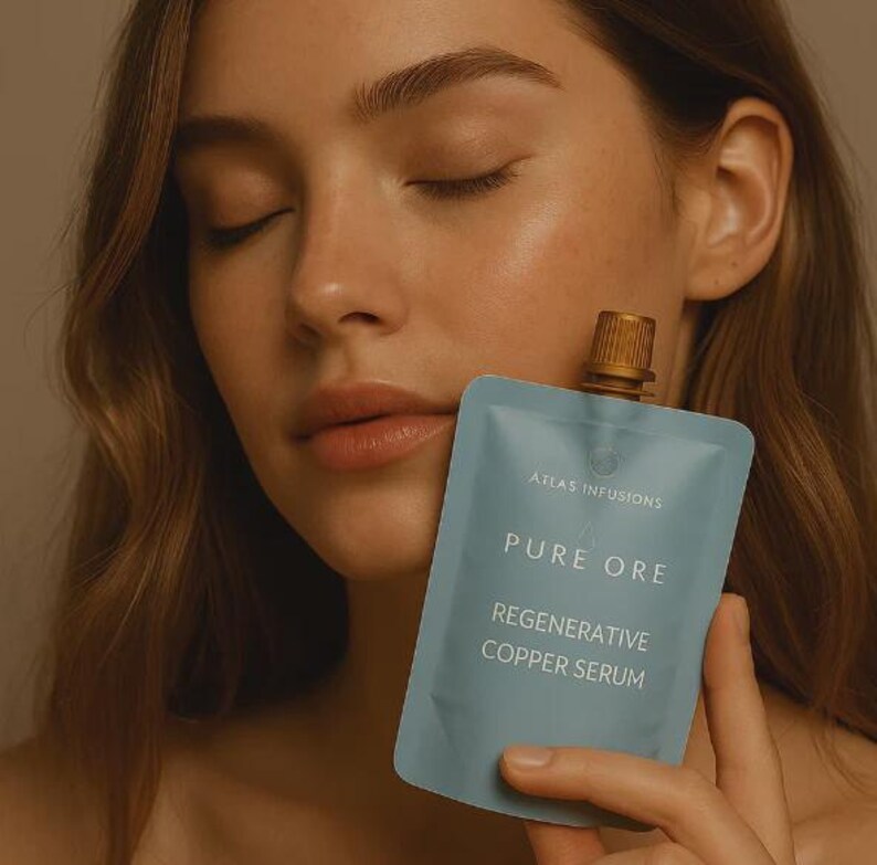 May include: A pale blue pouch with a gold cap, labelled "ATLAS INFUSIONS" and "PURE ORE REGENERATIVE COPPER SERUM." The pouch is held near a person's face, with their eyes closed.