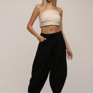 May include: A beige strapless tube top paired with black cropped trousers featuring a drawstring waist, side pockets, and a loose, tapered leg silhouette. The trousers end at the mid-calf, and the outfit is completed with beige slip-on shoes.