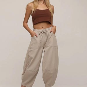 May include: A brown sleeveless crop top with a scoop neckline paired with beige wide-leg cropped pants featuring an elastic drawstring waistband, two front pockets, and a seam detail above the hem, worn with brown strappy gladiator sandals.
